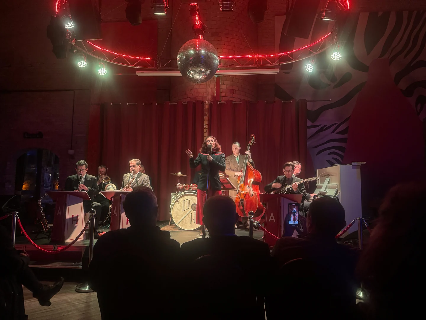 Eine Sängerin und Band spielen auf der Bühne des XELOR Kesselhauses; davor sitzen Gäste.