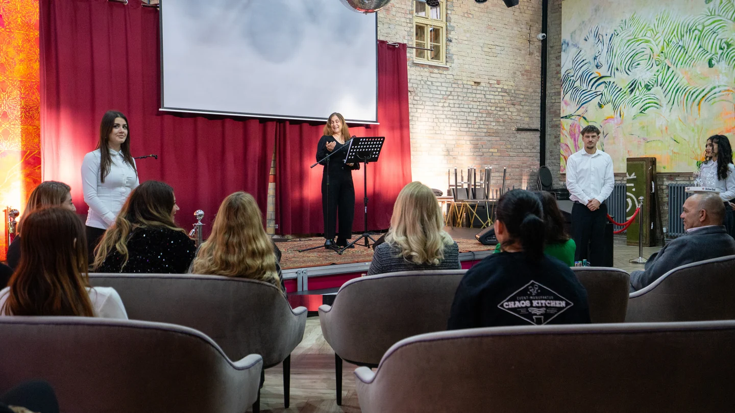 Eine Person steht am Mikrofon vor einer Leinwand; Gäste sitzen gegenüber der Bühne im XELOR Kesselhaus.