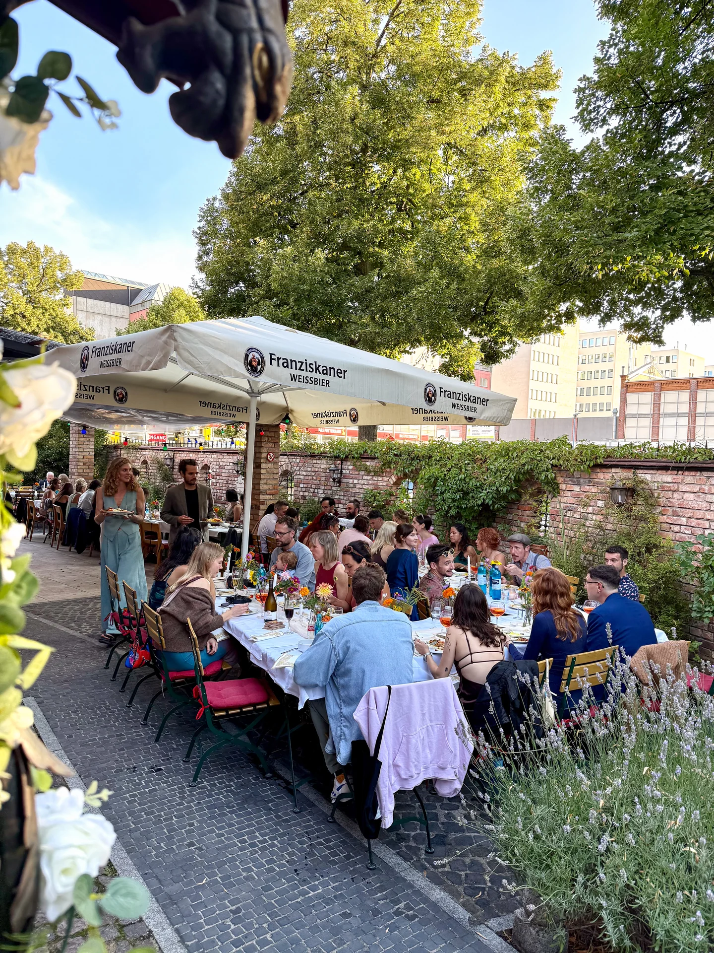Gäste an einer festlich gedeckten langen Tafel im begrünten Hof des XELOR Kesselhauses.